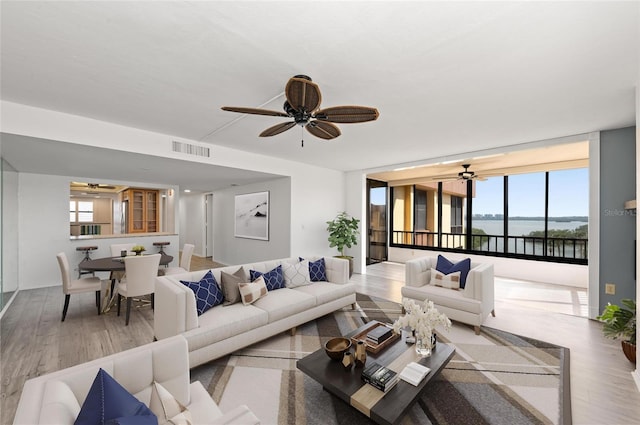 living room with floor to ceiling windows, a water view, hardwood / wood-style floors, and ceiling fan