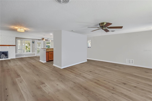 unfurnished living room featuring ceiling fan, a fireplace, a healthy amount of sunlight, and light wood-type flooring