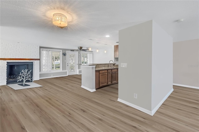 unfurnished living room featuring sink, ceiling fan, light hardwood / wood-style floors, a brick fireplace, and a textured ceiling