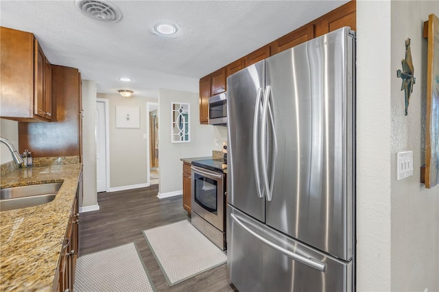 kitchen with sink, stainless steel appliances, light stone counters, a textured ceiling, and dark hardwood / wood-style flooring