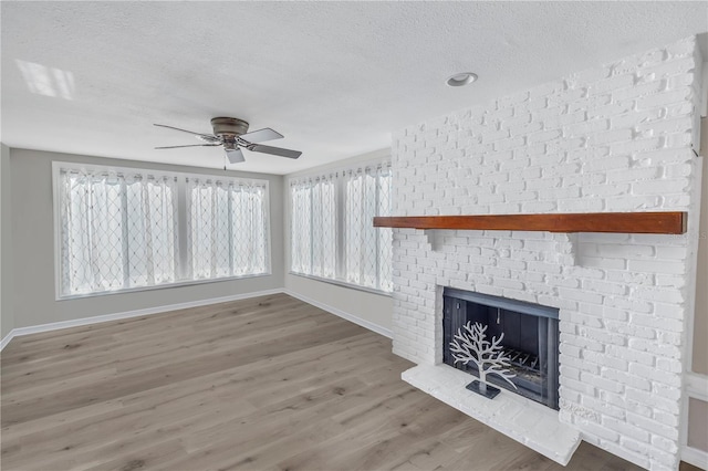 unfurnished living room with hardwood / wood-style flooring, ceiling fan, a brick fireplace, and a textured ceiling