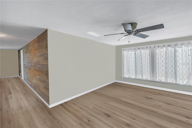 spare room featuring ceiling fan, wooden walls, light hardwood / wood-style floors, and a textured ceiling