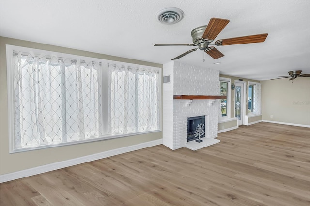 unfurnished living room featuring light hardwood / wood-style flooring, ceiling fan, a fireplace, and a textured ceiling