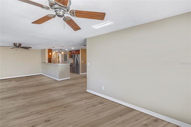 unfurnished living room featuring sink, a textured ceiling, ceiling fan, and light wood-type flooring