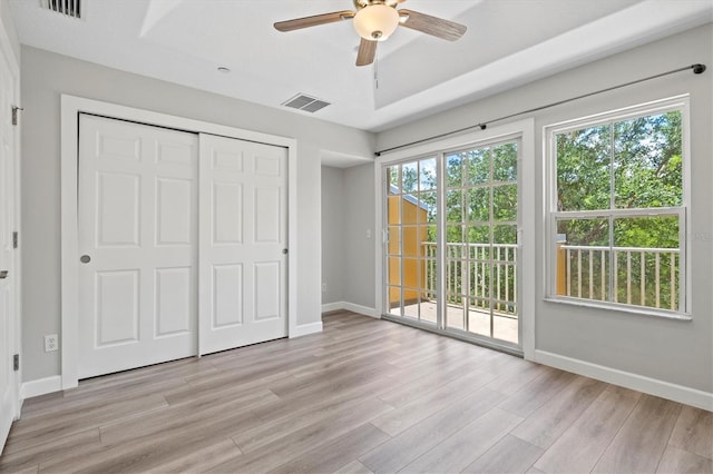 unfurnished bedroom featuring light hardwood / wood-style flooring, access to exterior, ceiling fan, a raised ceiling, and a closet