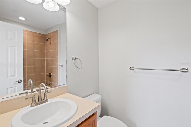 bathroom with tiled shower, vanity, and toilet