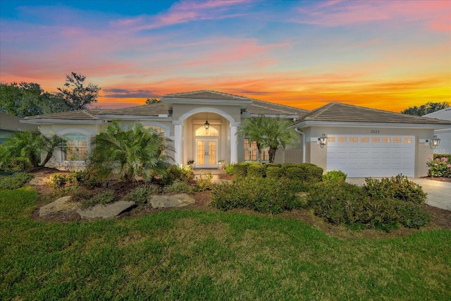 view of front of house with a garage, a lawn, and french doors