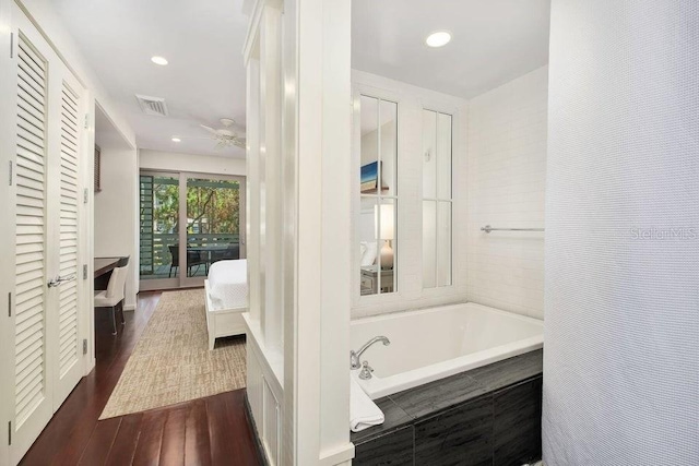 bathroom featuring ceiling fan, wood-type flooring, and tiled tub