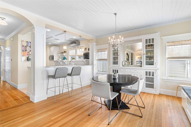 dining area featuring an inviting chandelier, light wood-type flooring, ornamental molding, and ornate columns