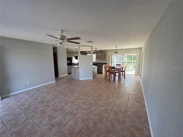 unfurnished living room featuring dark tile patterned floors, visible vents, baseboards, and a ceiling fan