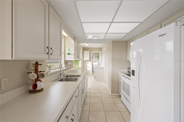 kitchen with sink, white appliances, light tile patterned floors, white cabinetry, and washer / dryer