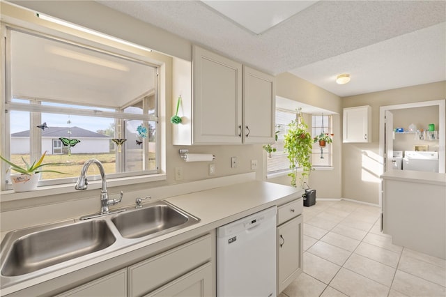 kitchen featuring sink, light tile patterned floors, dishwasher, washing machine and dryer, and white cabinets