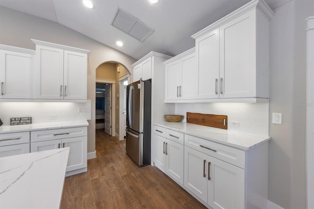 kitchen with lofted ceiling, stainless steel refrigerator, white cabinetry, dark hardwood / wood-style floors, and light stone countertops