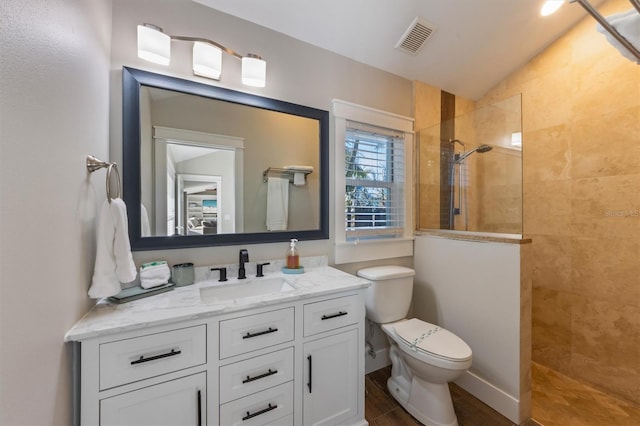 bathroom featuring vanity, lofted ceiling, toilet, and tiled shower