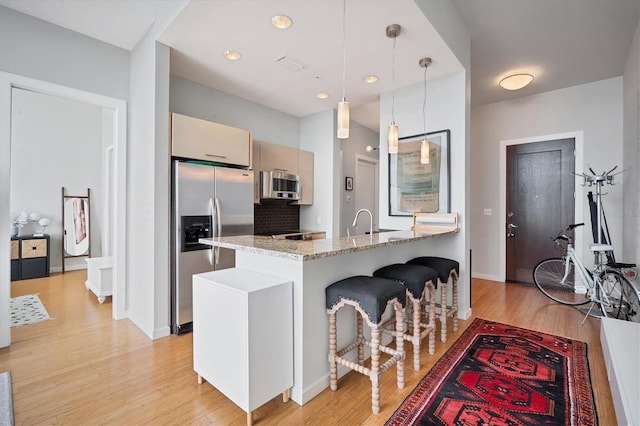 kitchen with a kitchen bar, light wood-type flooring, appliances with stainless steel finishes, pendant lighting, and light stone countertops