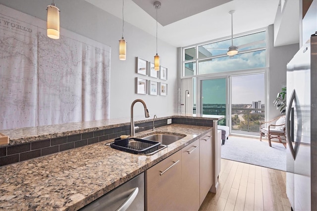 kitchen with sink, appliances with stainless steel finishes, hanging light fixtures, floor to ceiling windows, and light stone counters