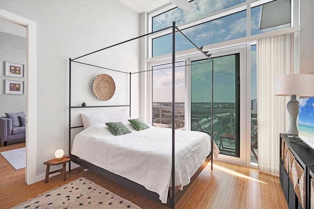 bedroom with access to outside, hardwood / wood-style floors, a wall of windows, and a towering ceiling