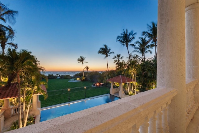 pool at dusk with a water view and a yard