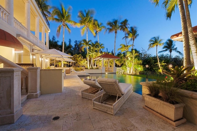 patio terrace at dusk featuring a gazebo and exterior bar