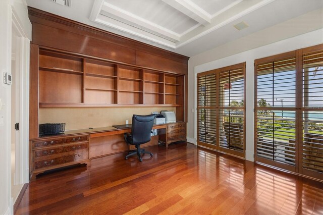 unfurnished office featuring hardwood / wood-style flooring, built in desk, and beamed ceiling