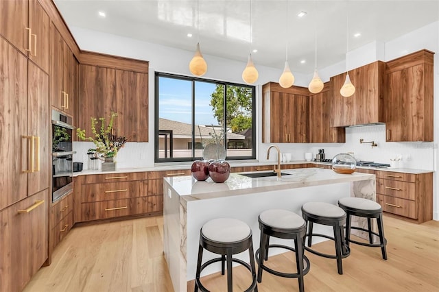 kitchen with tasteful backsplash, brown cabinets, a sink, and light wood-style flooring