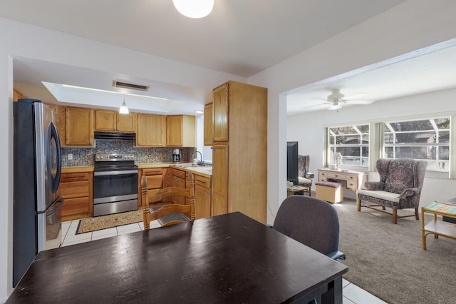 kitchen with backsplash, stainless steel appliances, a tray ceiling, decorative light fixtures, and light colored carpet