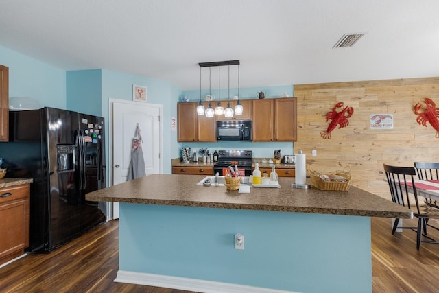 kitchen featuring pendant lighting, wooden walls, an island with sink, black appliances, and dark wood-type flooring