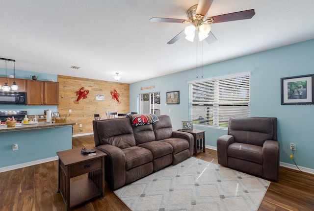 living room featuring hardwood / wood-style flooring, ceiling fan, and wood walls