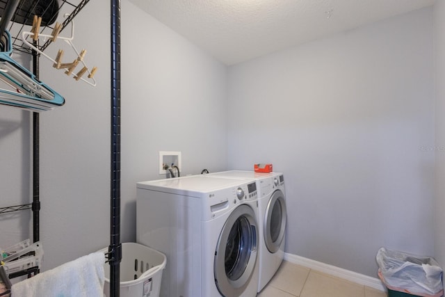 laundry area with independent washer and dryer, a textured ceiling, and light tile patterned flooring