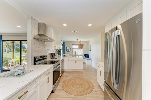 kitchen with hanging light fixtures, wall chimney range hood, kitchen peninsula, stainless steel appliances, and white cabinets