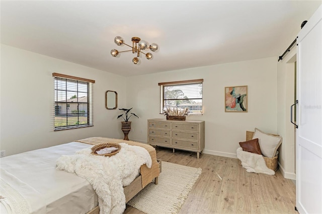 bedroom with a notable chandelier, a barn door, multiple windows, and light hardwood / wood-style flooring