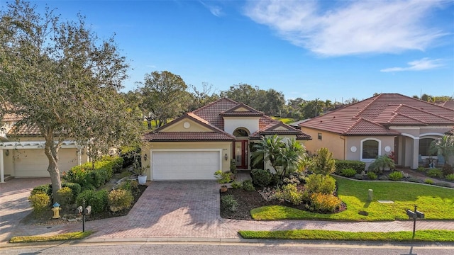 mediterranean / spanish house featuring decorative driveway, stucco siding, an attached garage, and a tiled roof