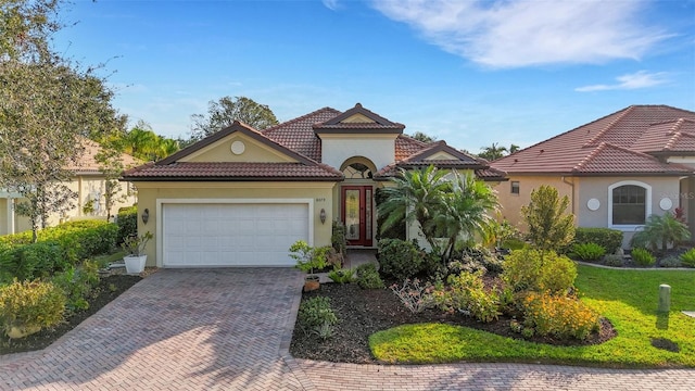 mediterranean / spanish-style home featuring a front lawn, a tiled roof, stucco siding, decorative driveway, and an attached garage