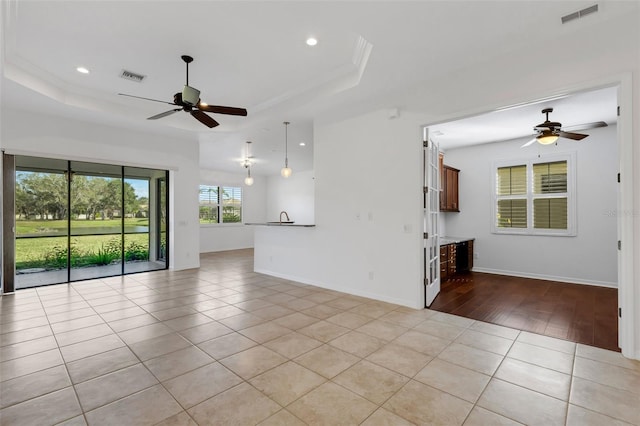 unfurnished living room featuring ceiling fan, a raised ceiling, and light tile patterned floors