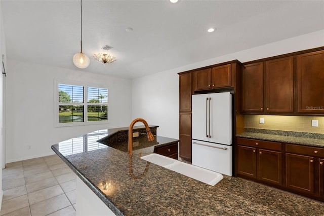 kitchen with sink, dark stone countertops, backsplash, hanging light fixtures, and white fridge