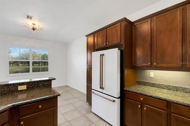 kitchen with tasteful backsplash, light tile patterned floors, high end white fridge, and dark stone counters