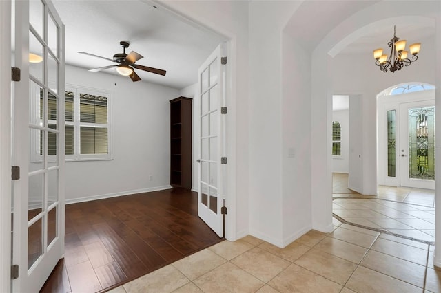 tiled foyer entrance with french doors and ceiling fan with notable chandelier