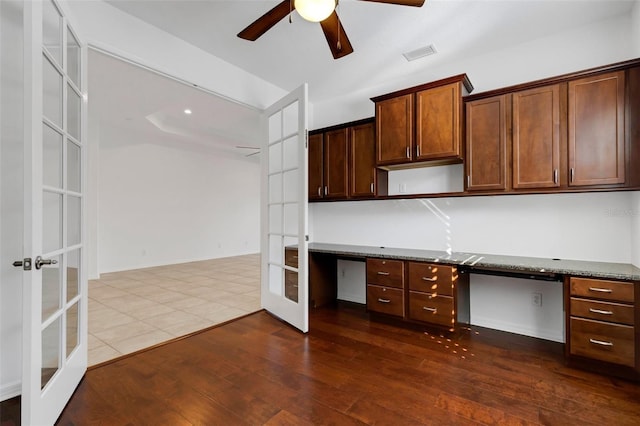 kitchen featuring french doors, dark wood-type flooring, built in desk, ceiling fan, and dark stone counters