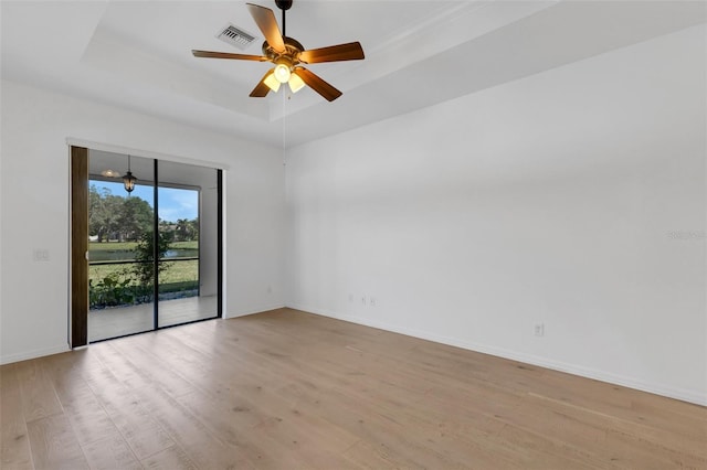 empty room with a tray ceiling, ceiling fan, and light wood-type flooring