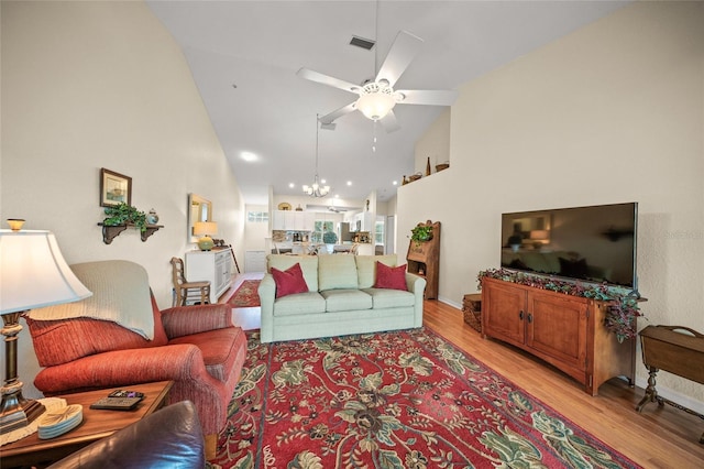 living room with high vaulted ceiling, ceiling fan with notable chandelier, and light hardwood / wood-style flooring