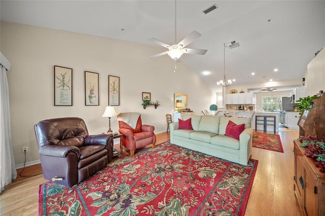 living room with high vaulted ceiling, ceiling fan with notable chandelier, and light hardwood / wood-style floors