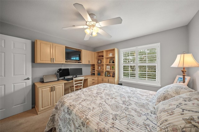 bedroom featuring built in desk, light colored carpet, and ceiling fan