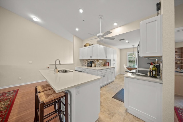 kitchen with a center island with sink, a breakfast bar area, light countertops, white cabinets, and a sink