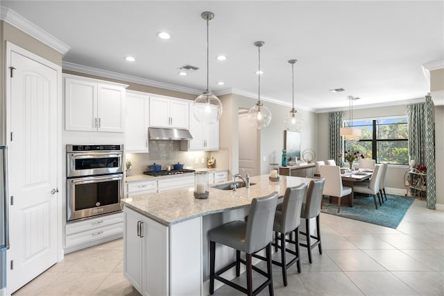 kitchen with appliances with stainless steel finishes, pendant lighting, an island with sink, white cabinets, and light stone counters