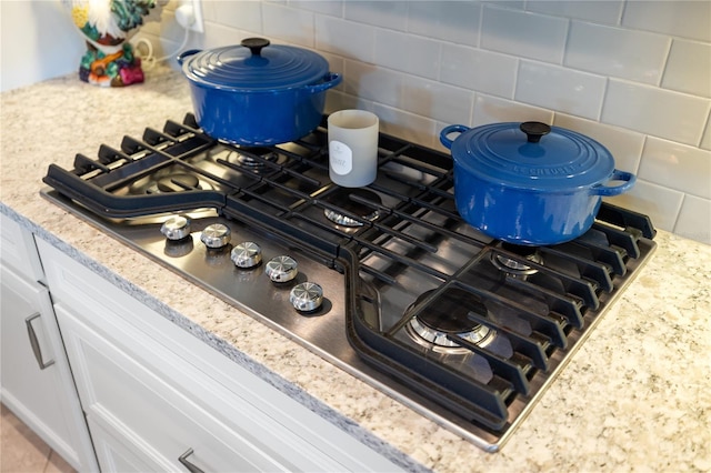 room details with tasteful backsplash, light stone counters, stainless steel gas stovetop, and white cabinets