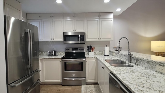 kitchen with sink, appliances with stainless steel finishes, white cabinetry, hardwood / wood-style floors, and light stone counters