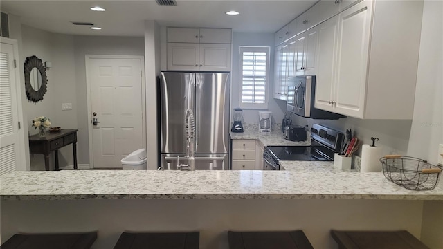 kitchen with a breakfast bar, white cabinetry, stainless steel appliances, light stone countertops, and kitchen peninsula