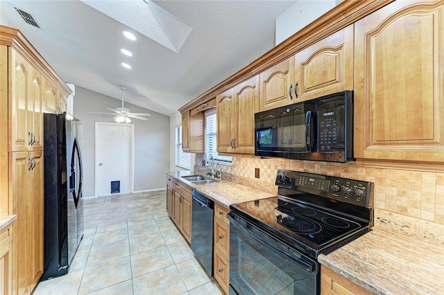 kitchen with sink, vaulted ceiling, light tile patterned floors, light stone countertops, and black appliances