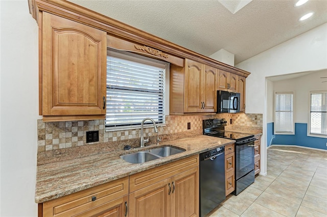 kitchen with vaulted ceiling, sink, light tile patterned floors, light stone counters, and black appliances