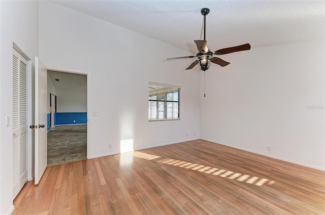 empty room with ceiling fan, high vaulted ceiling, light hardwood / wood-style flooring, and a textured ceiling